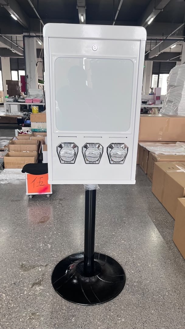 Weißer Postkartenautomat V3 mit drei Schächten auf schwarzem Standfuß in der Produktionshalle